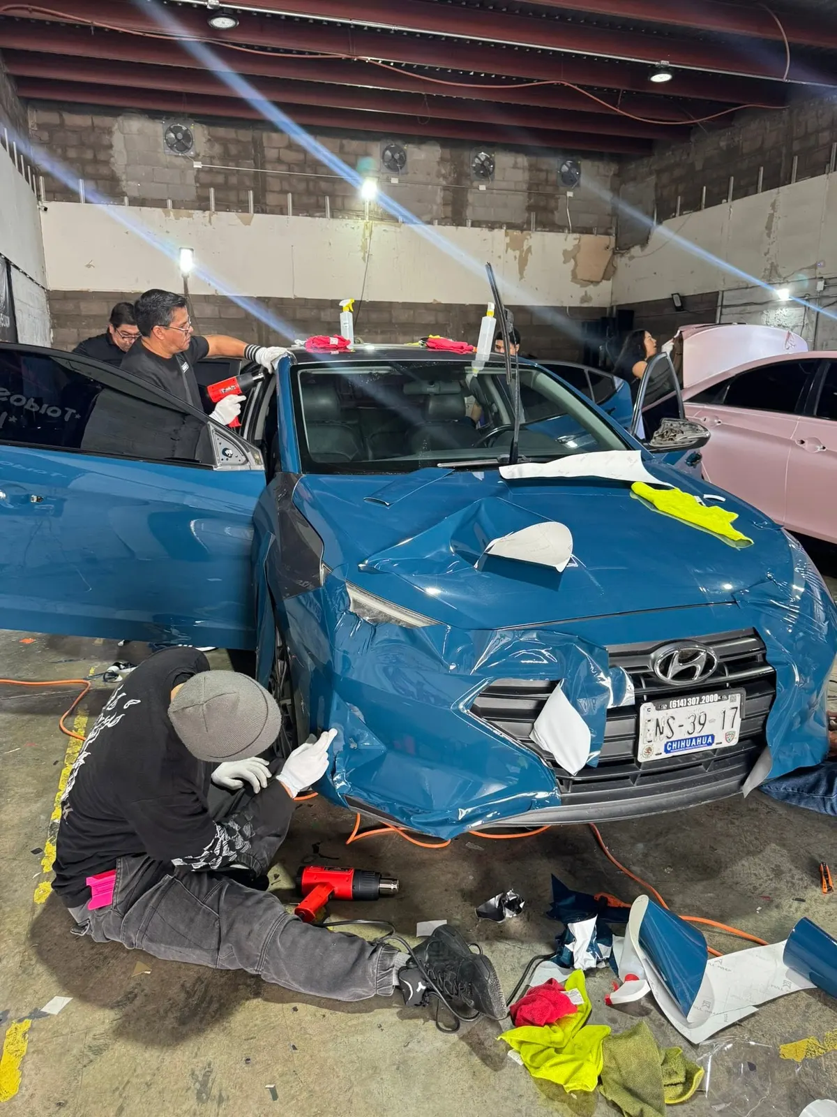 Alumnos instalando wrap azul en un Hyundai Elantra durante el curso