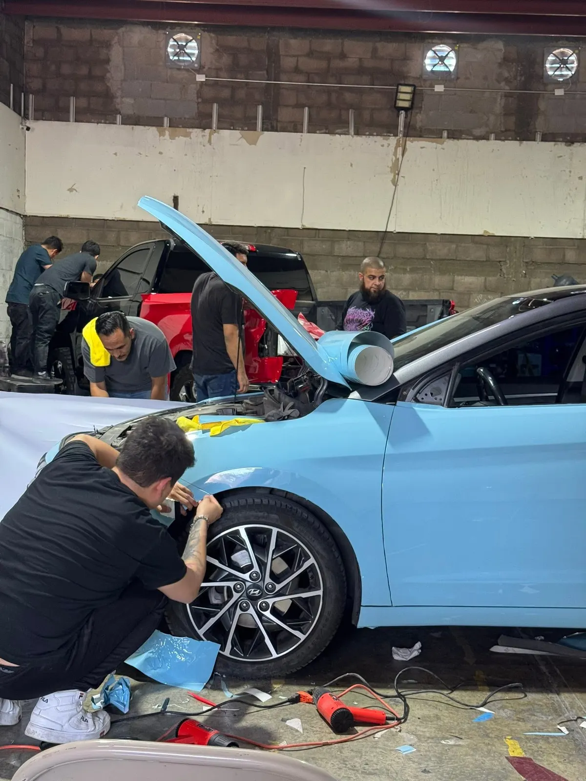 Alumnos instalando wrap celeste en un Hyundai Elantra durante el curso