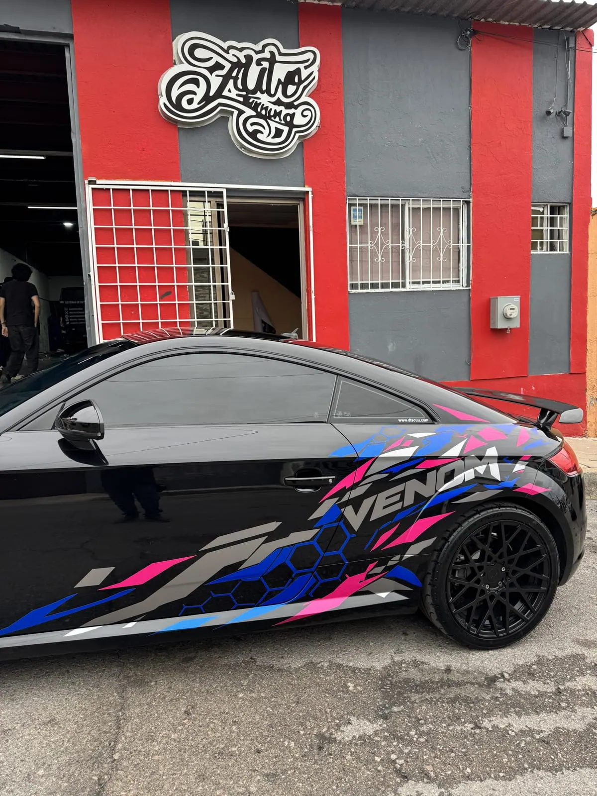 Audi TT negro con diseño personalizado VENOM en rosa y azul, frente al taller de Auto Tuning Shop