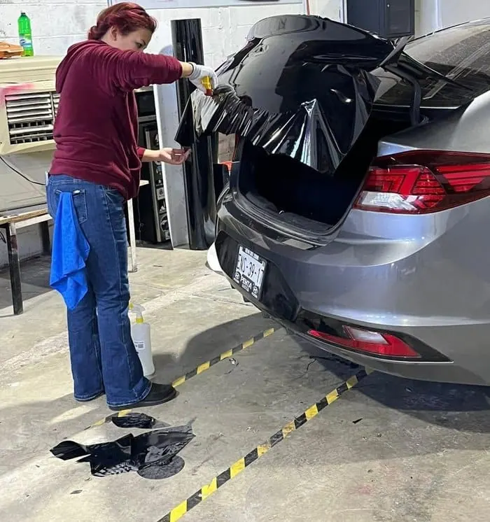 Alumna instalando wrap negro en la cajuela de un sedán