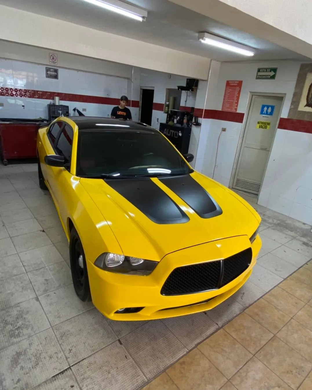 Dodge Charger amarillo con franjas negras dentro del segundo taller