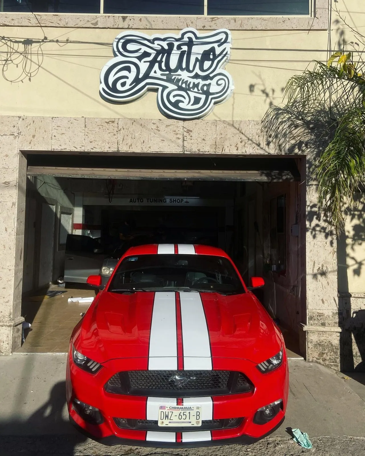 Ford Mustang rojo con franjas blancas en la entrada del segundo taller